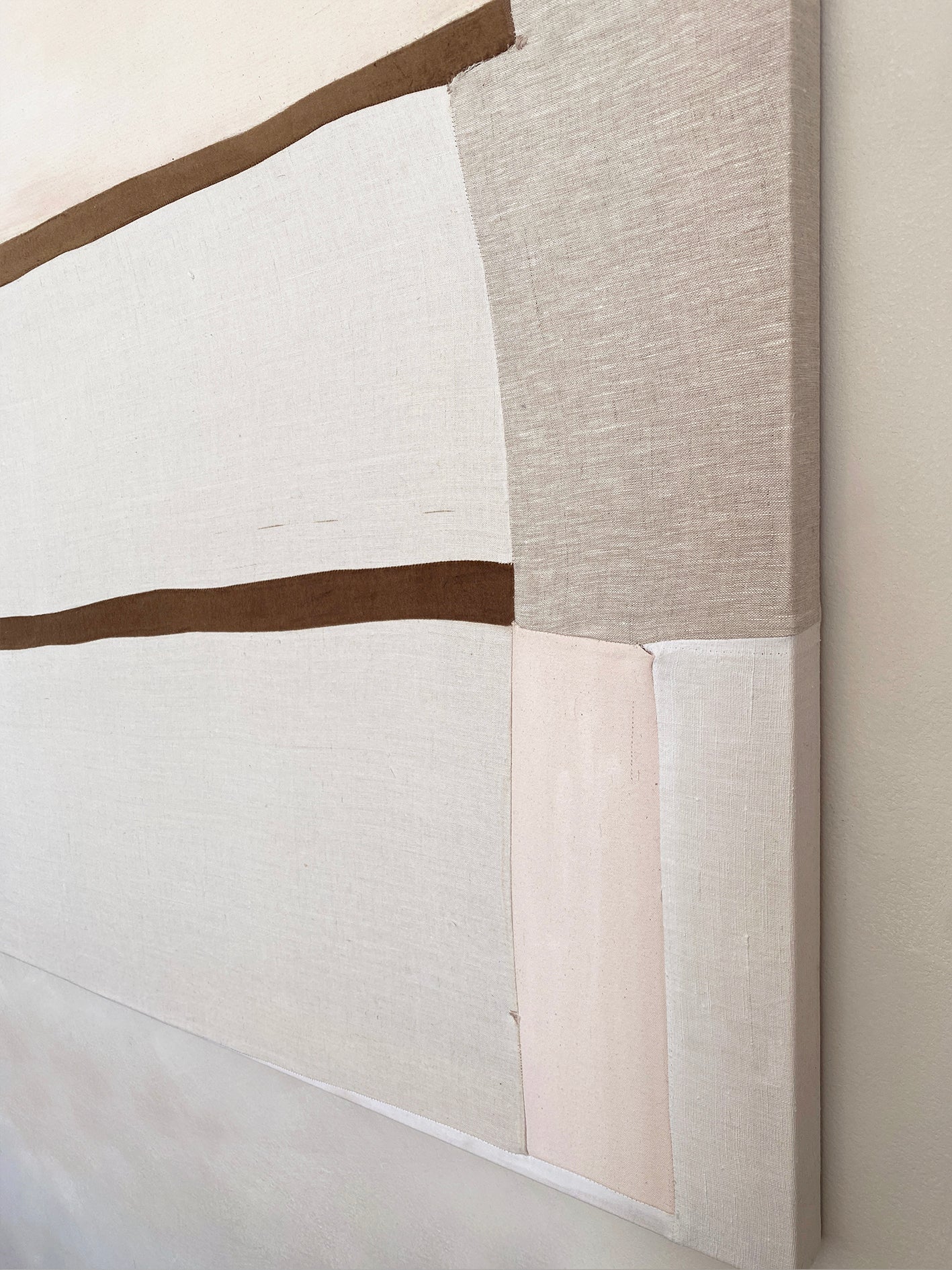 a large abstract artwork with neutral fabric painterly elements and two strips of brown velvet