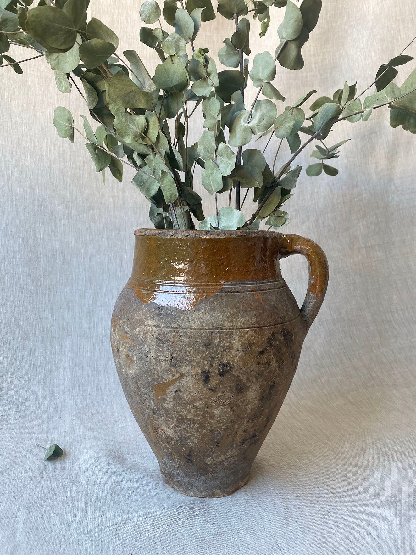 an antique olive drip vase with a single handle and dark mustard glaze