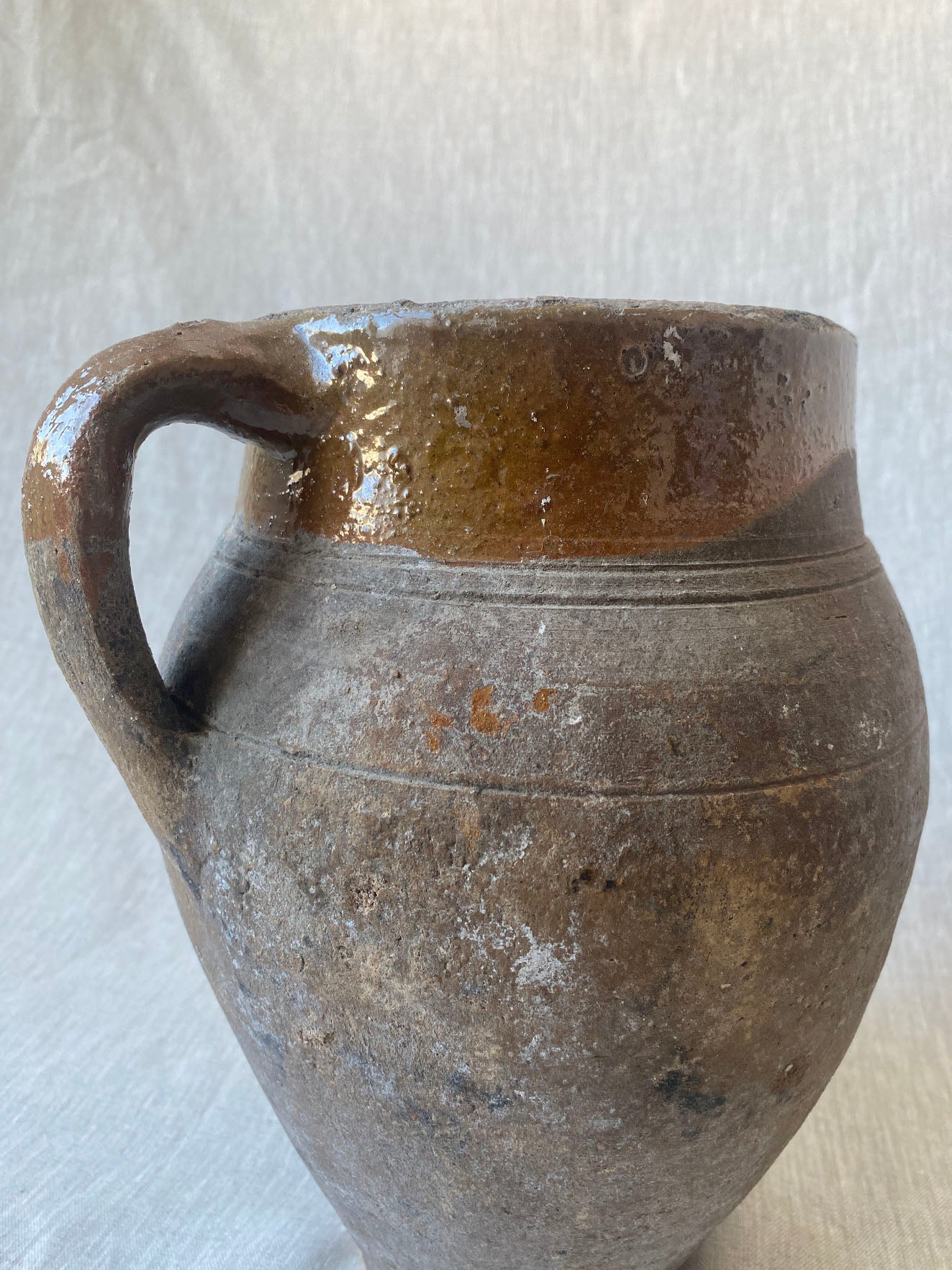 an antique olive drip vase with a single handle and dark mustard glaze