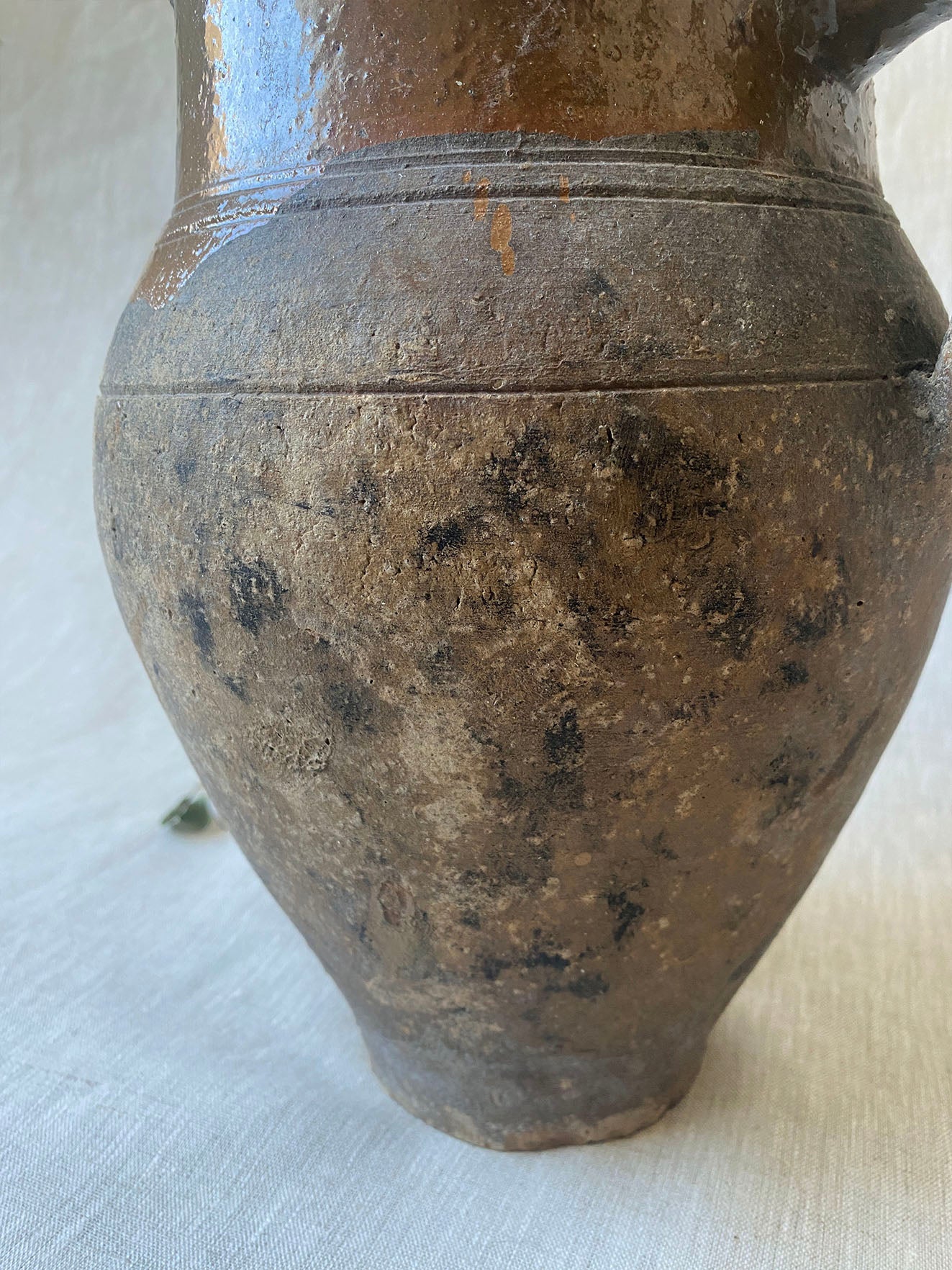 an antique olive drip vase with a single handle and dark mustard glaze