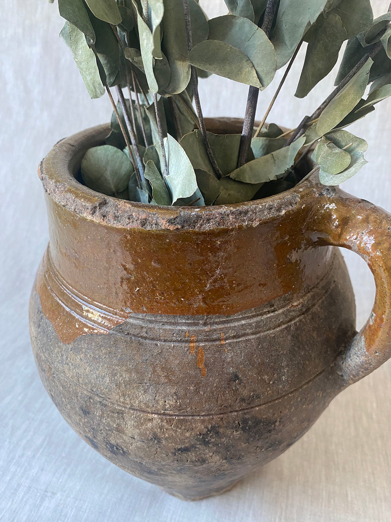 an antique olive drip vase with a single handle and dark mustard glaze