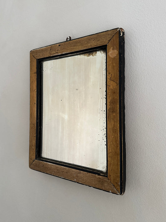 a small antique gentleman's shaving mirror in a natural wood and black frame with some light frosting