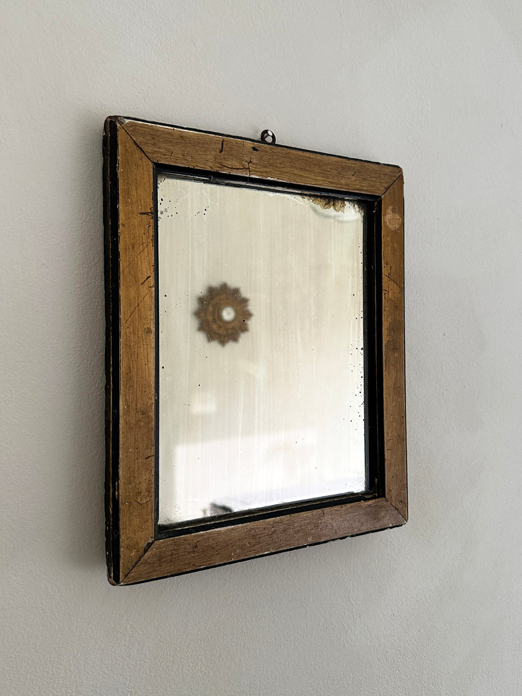 a small antique gentleman's shaving mirror in a natural wood and black frame with some light frosting