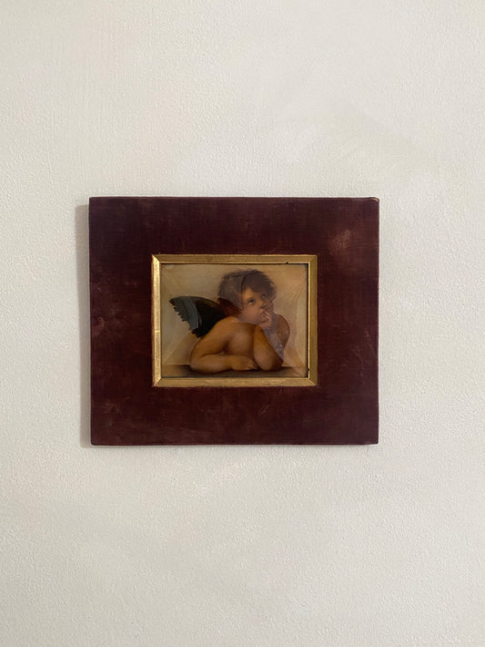 a winged cherub in a dark brown velvet and gilt frame