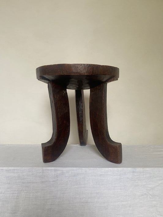 an antique hand-carved wooden stool with three sculptural legs and a round concave seat