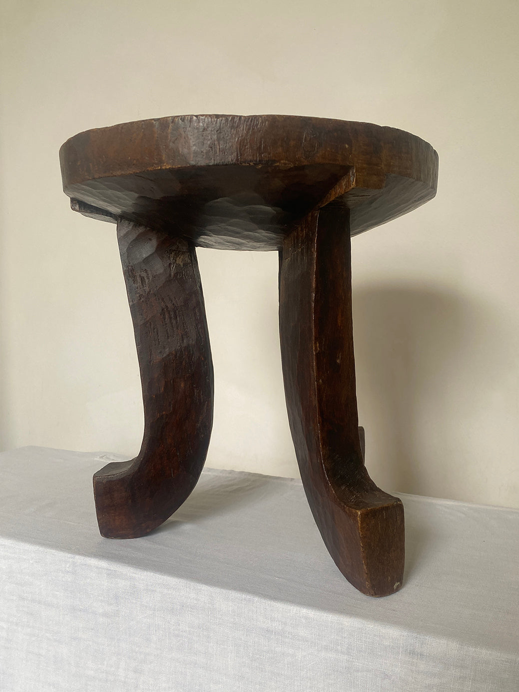 an antique hand-carved wooden stool with three sculptural legs and a round concave seat