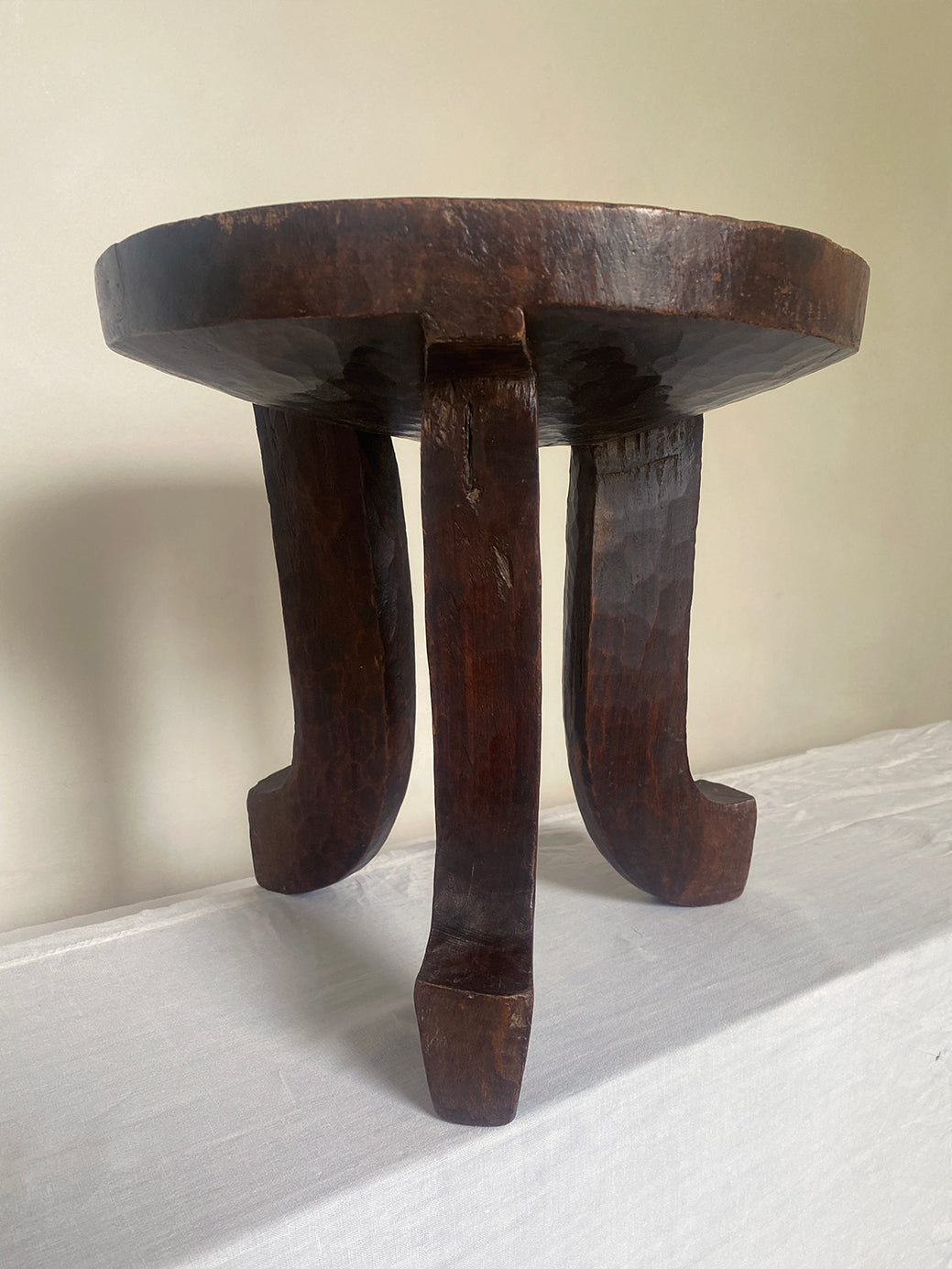 an antique hand-carved wooden stool with three sculptural legs and a round concave seat