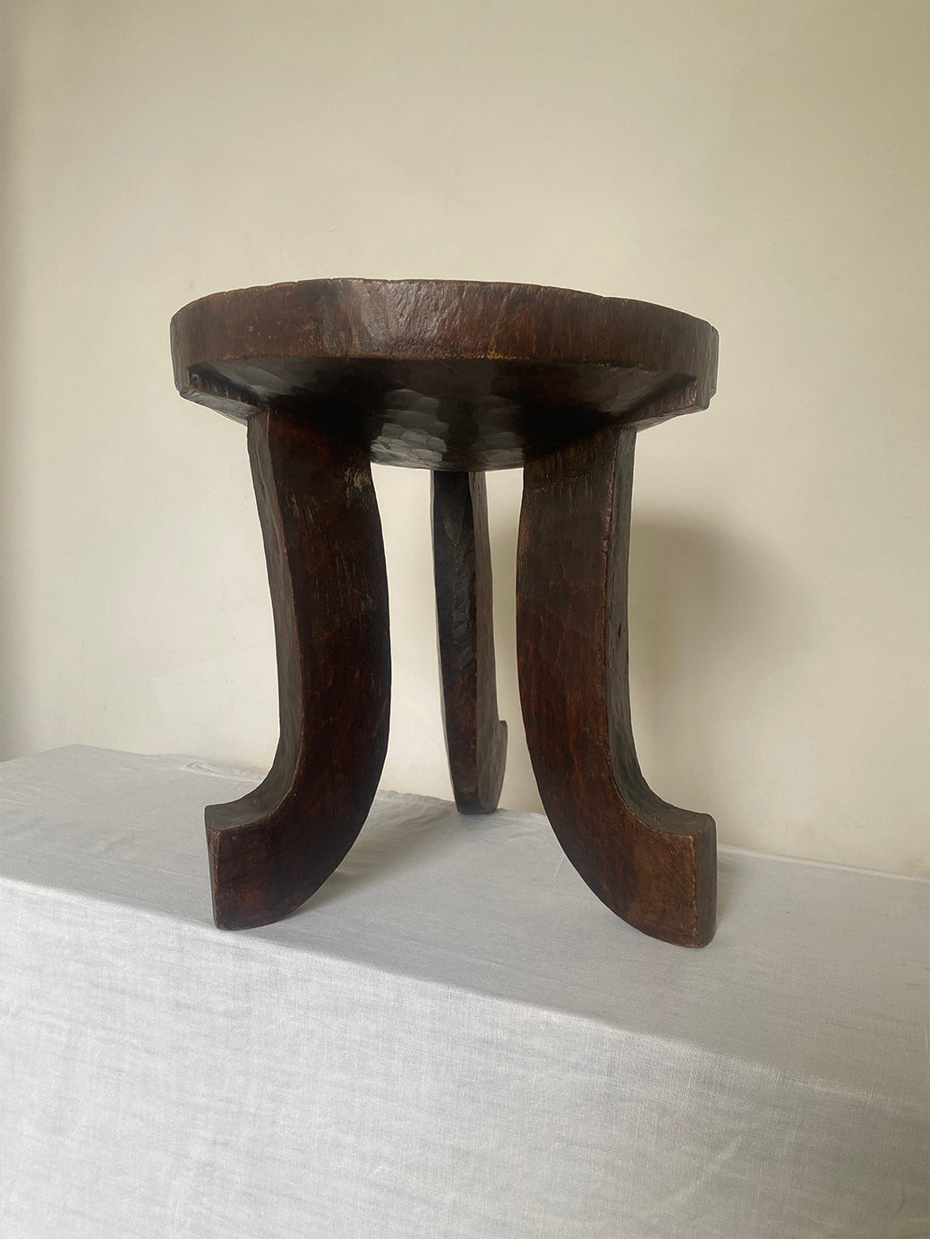 an antique hand-carved wooden stool with three sculptural legs and a round concave seat