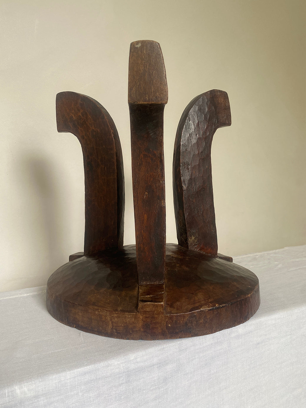 an antique hand-carved wooden stool with three sculptural legs and a round concave seat