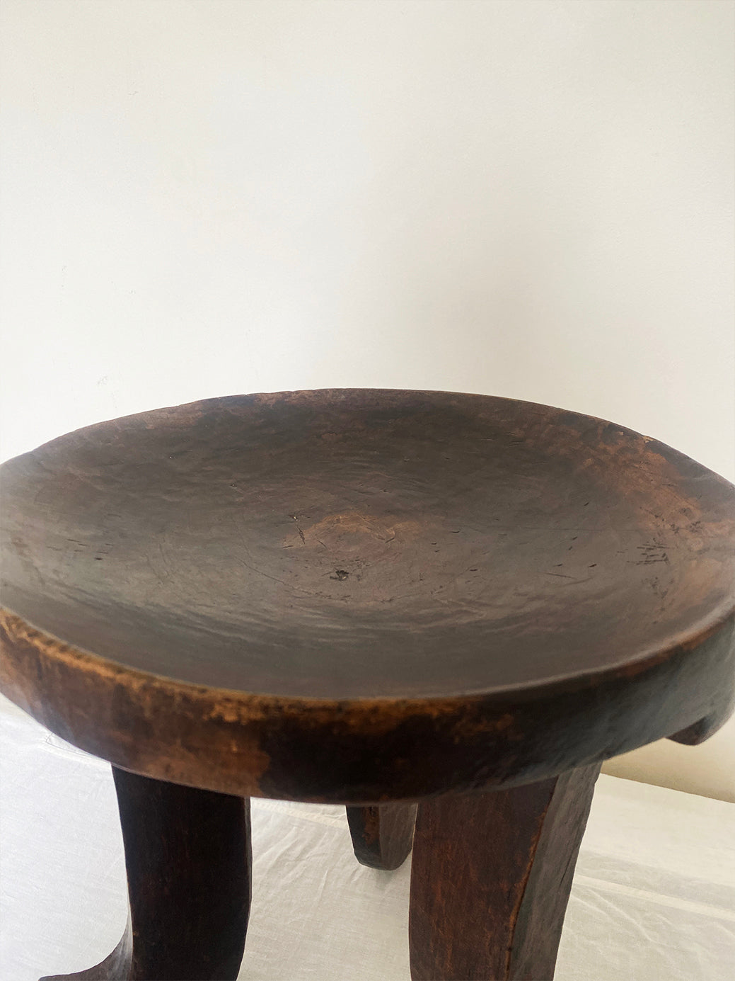 an antique hand-carved wooden stool with three sculptural legs and a round concave seat