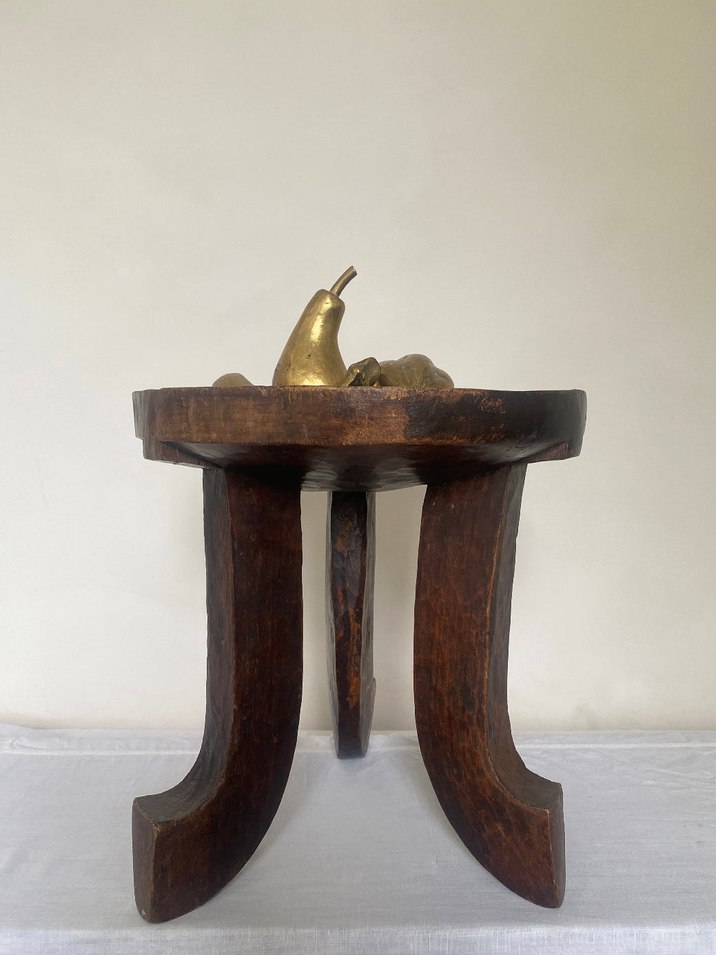 an antique hand-carved wooden stool with three sculptural legs and a round concave seat