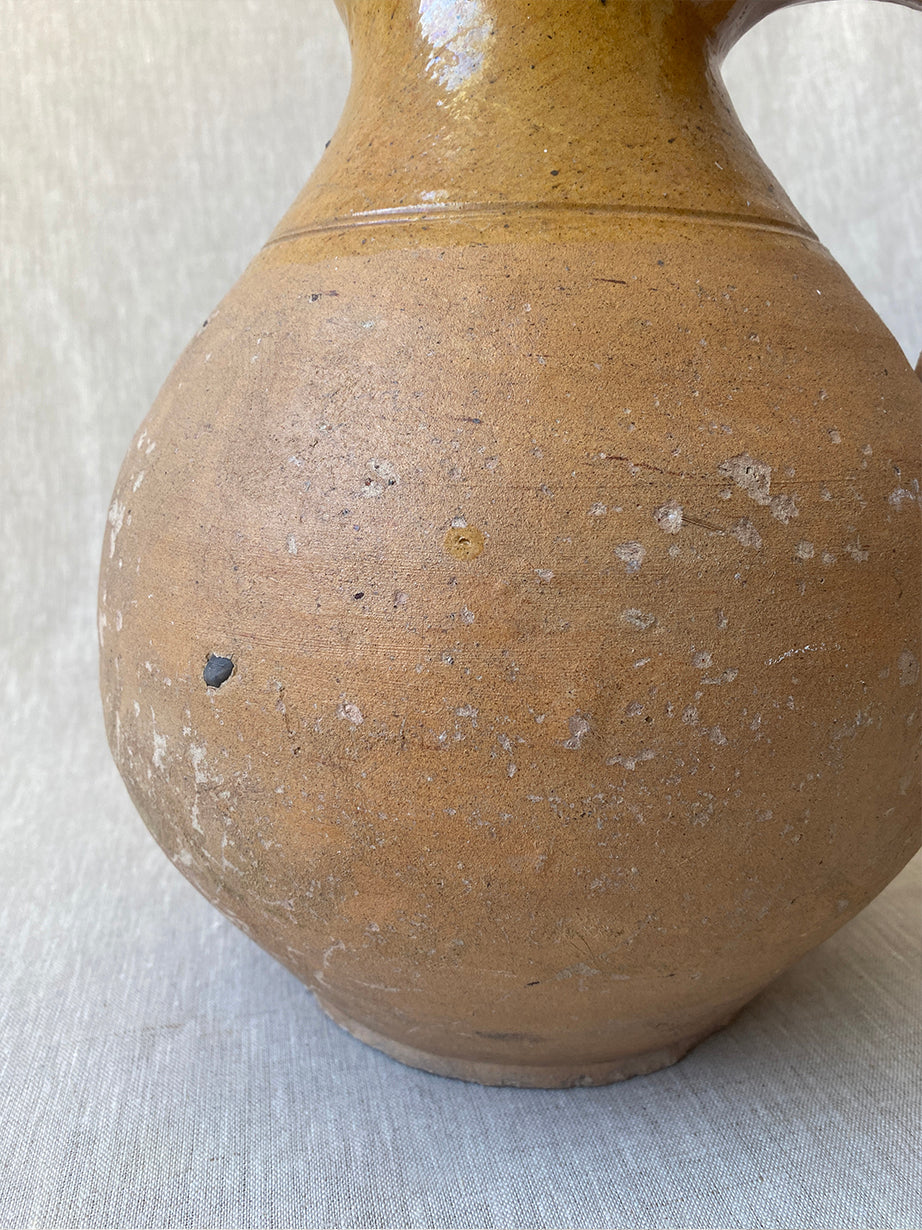 an antique earthenware jug with a curved handle and mustard yellow glaze