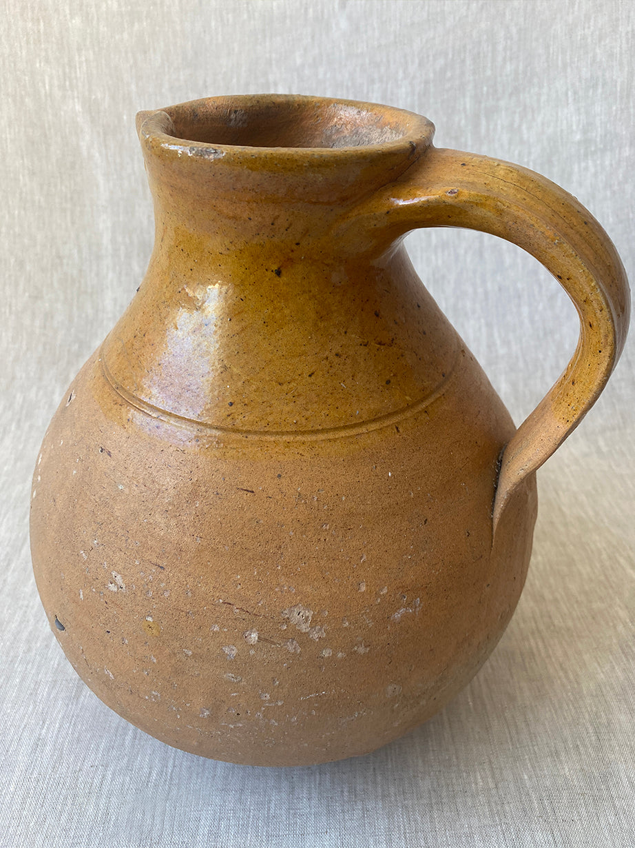 an antique earthenware jug with a curved handle and mustard yellow glaze