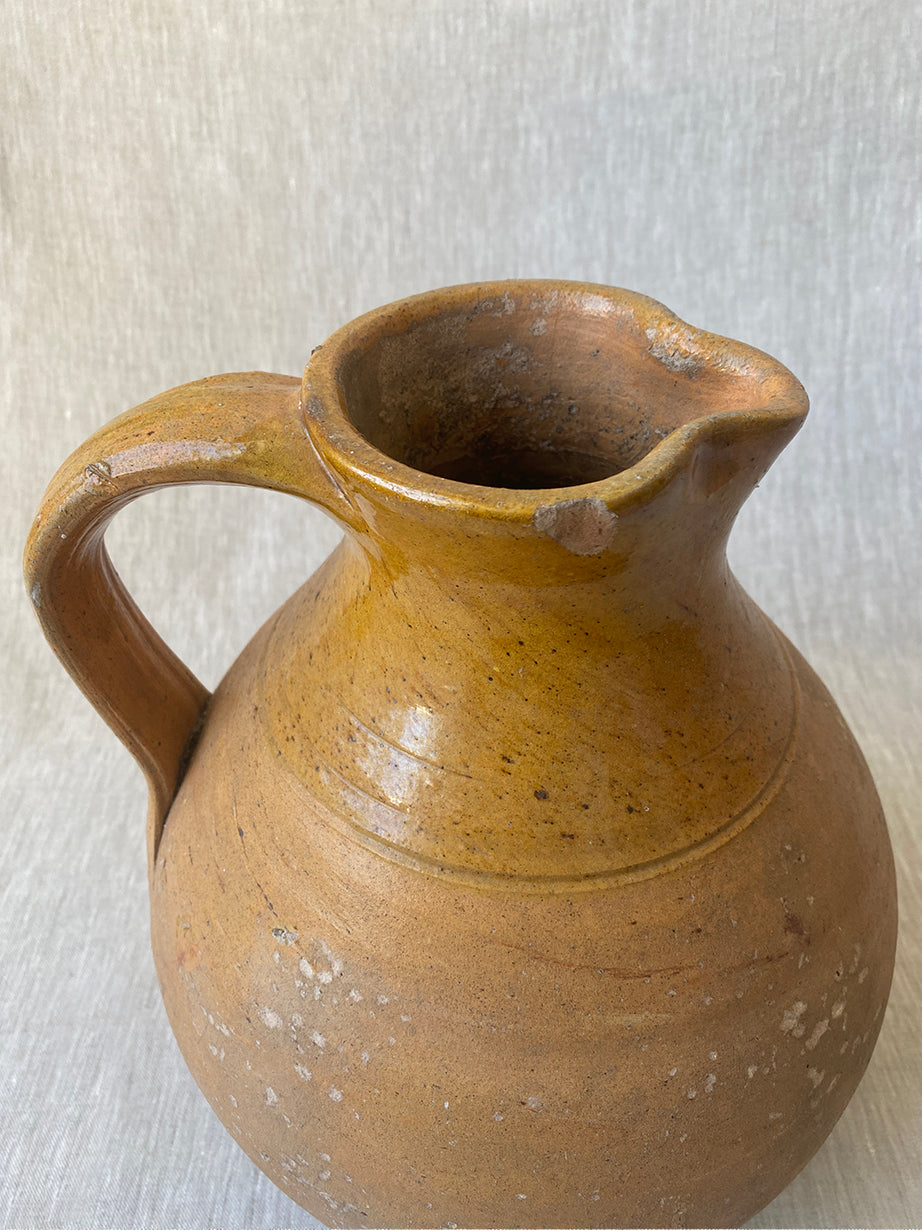 an antique earthenware jug with a curved handle and mustard yellow glaze