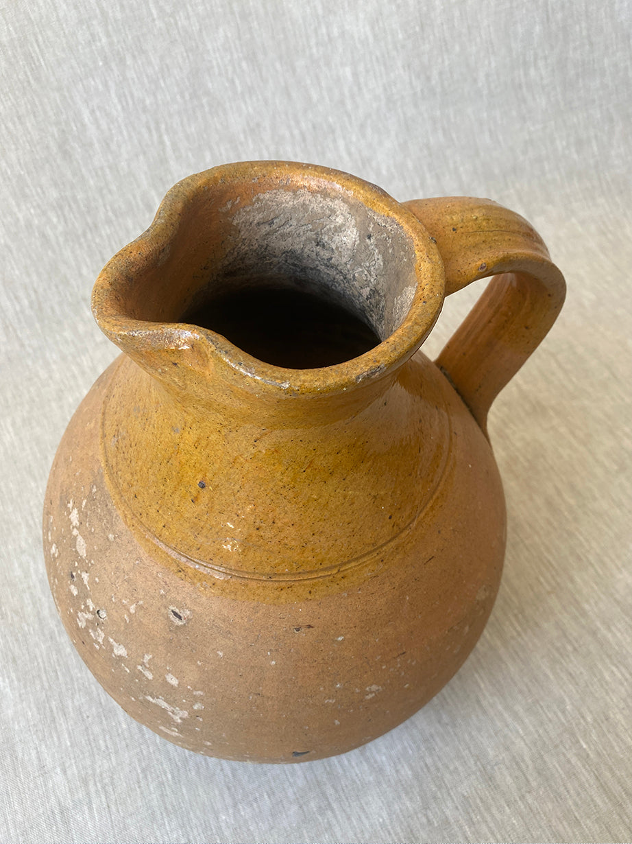 an antique earthenware jug with a curved handle and mustard yellow glaze