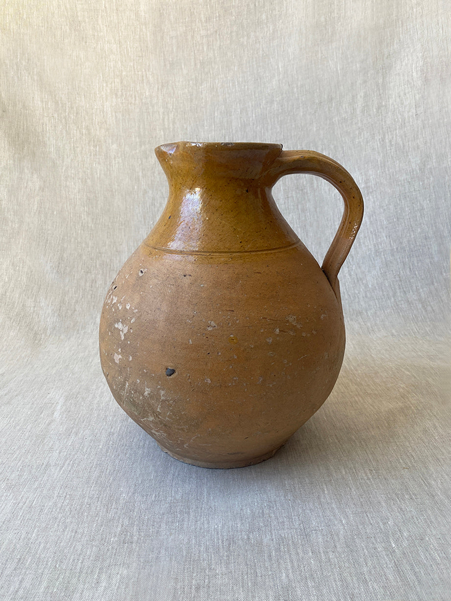 an antique earthenware jug with a curved handle and mustard yellow glaze